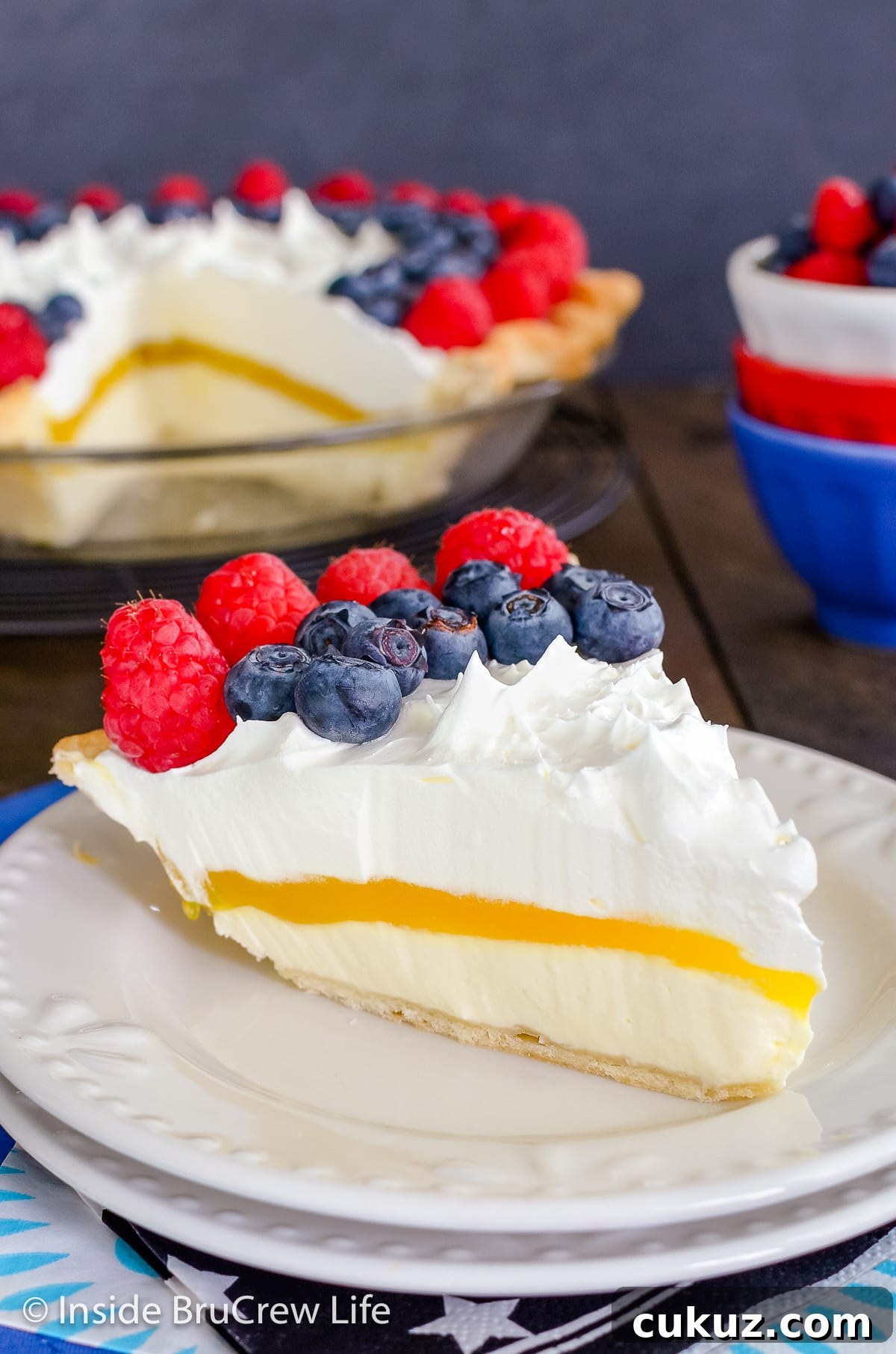 A slice of lemon pie topped with berries on a white plate.