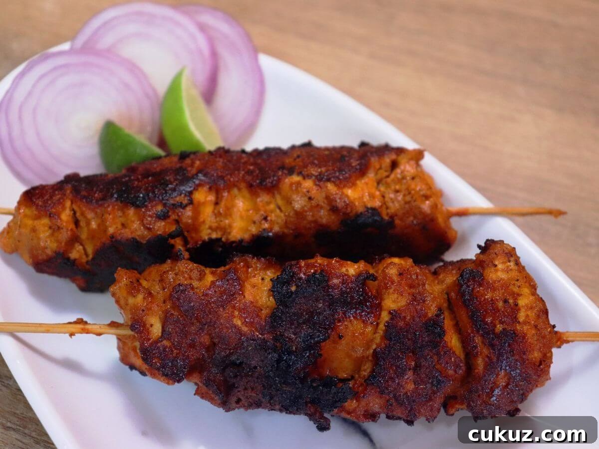 Chicken Boti Kabab Recipe: Tender Grilled Boti Kebab Guide 2 close-up of boti kebab in a skewer served on a plate with onion slices and a lemon wedge on the side.