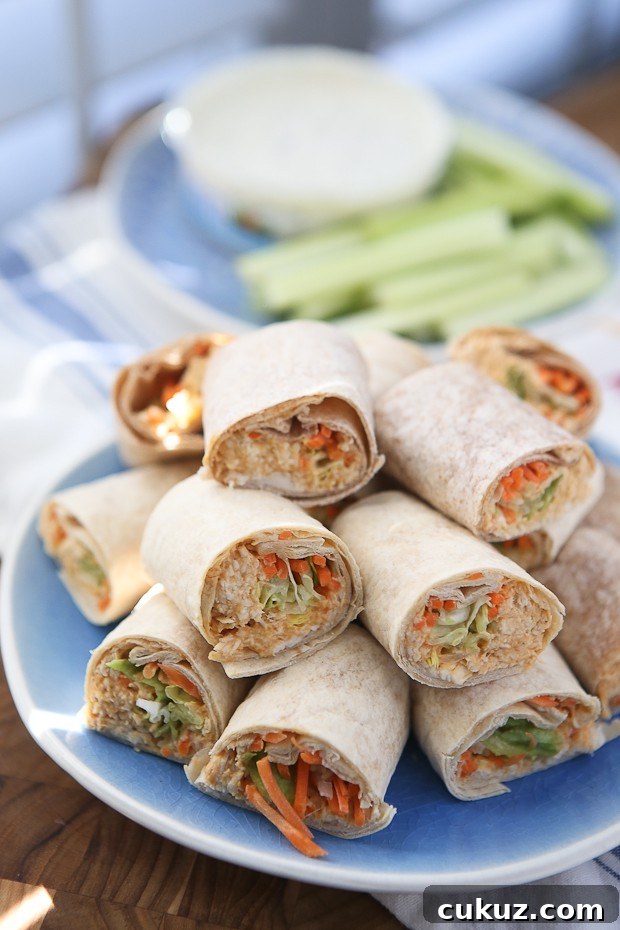 Buffalo Hummus Chicken Salad Roll Ups plate of wraps with various vegetables and chicken salad cut in half and stacked on each other