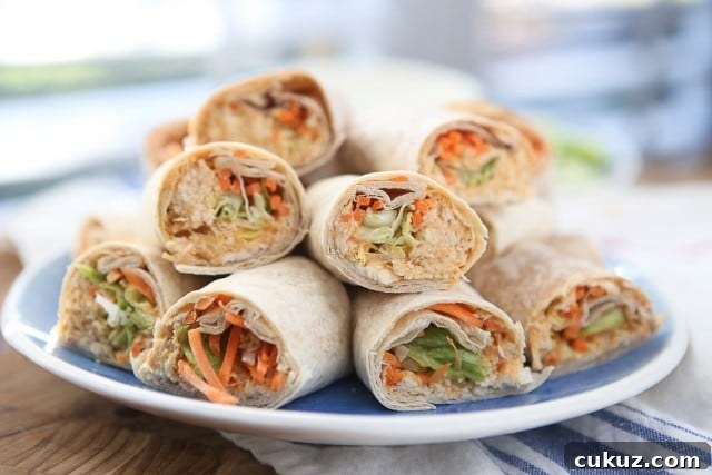Buffalo Hummus Chicken Salad Roll Ups plate of wraps with various vegetables and chicken salad cut in half and stacked on each other