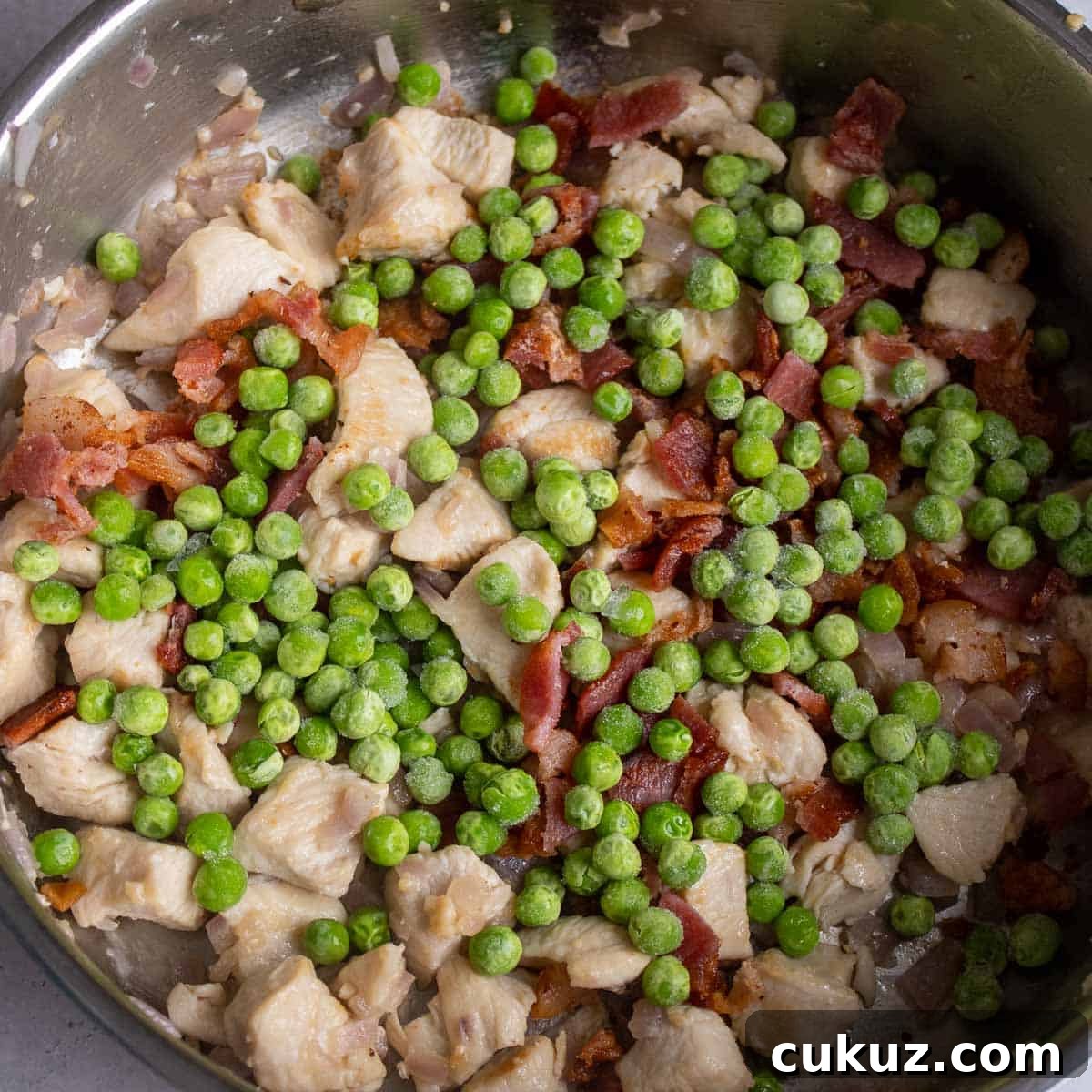 Peas and cooked bacon added to the cooking chicken