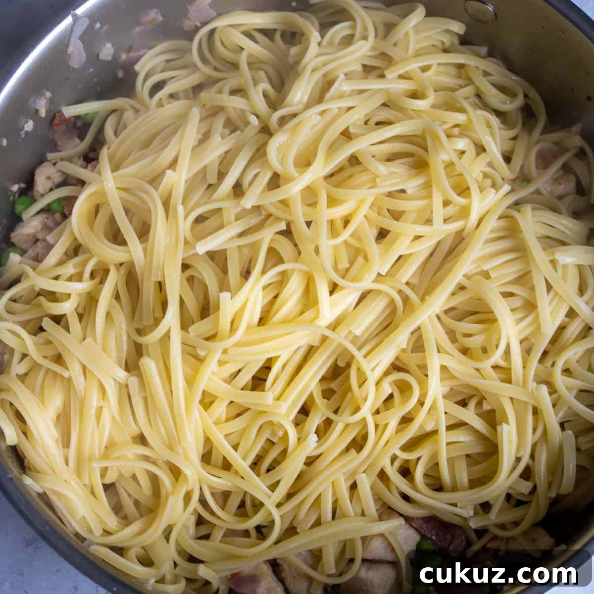 Adding the cooked linguine pasta to the chicken mixture.