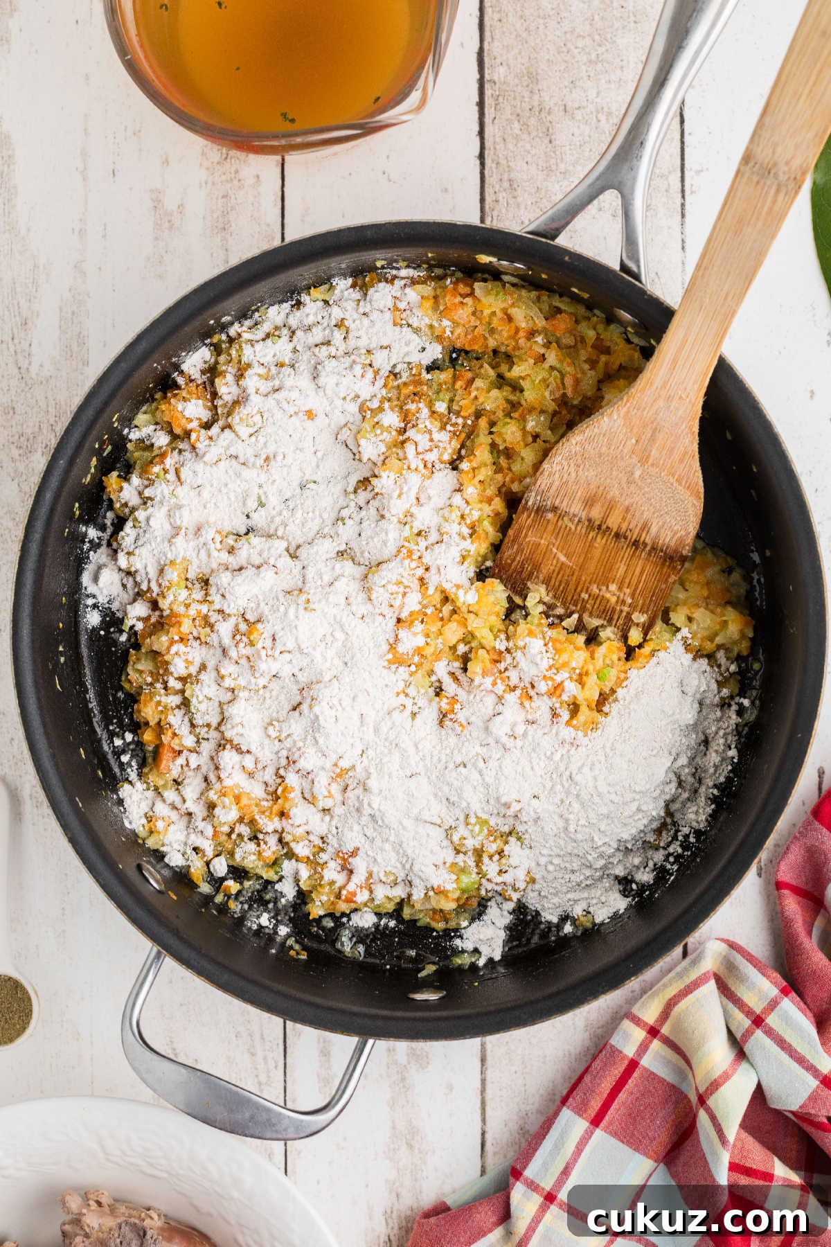 Flour added to a skillet of cooking vegetables.