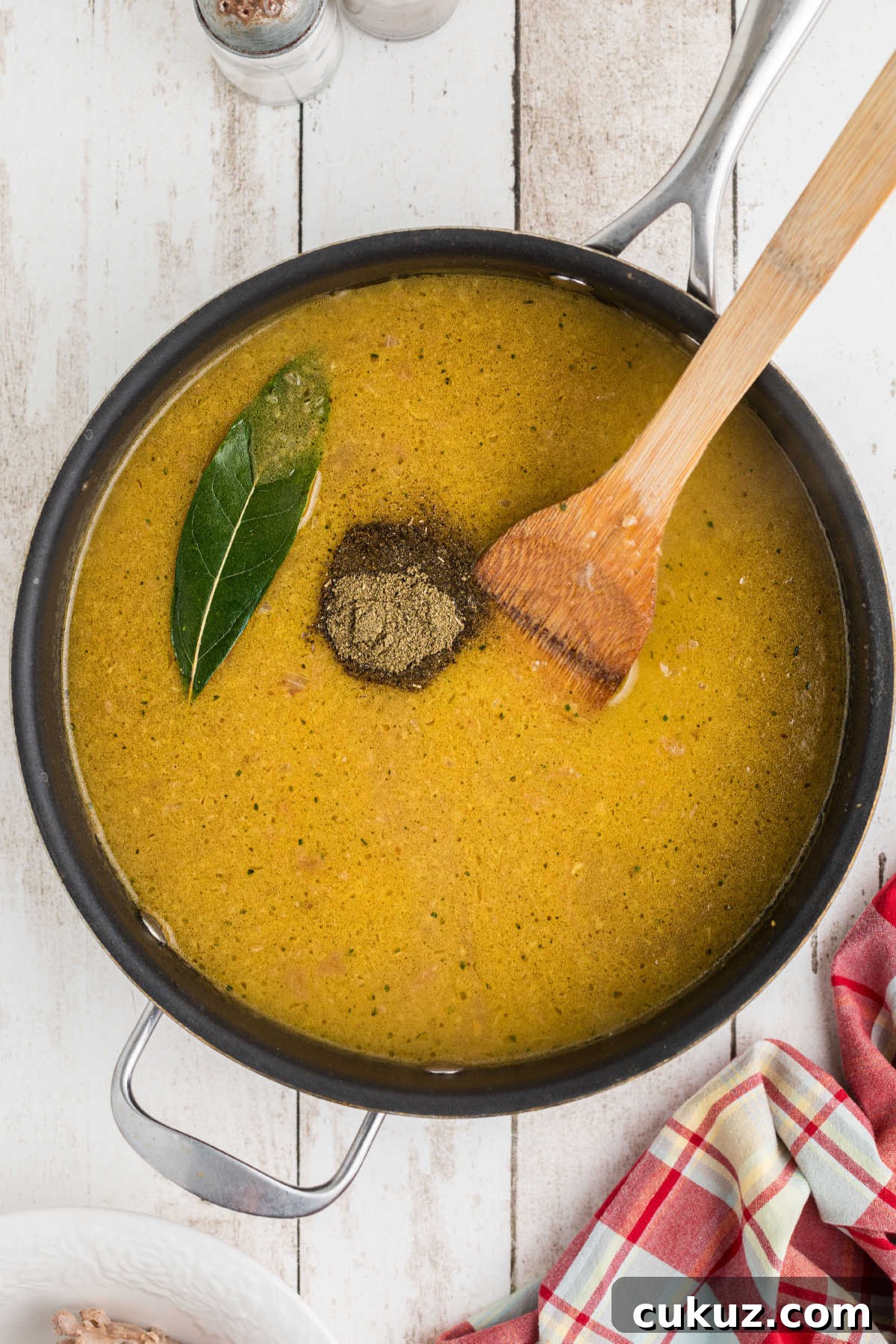 Seasonings added to a skillet of gravy with a bay leaf.