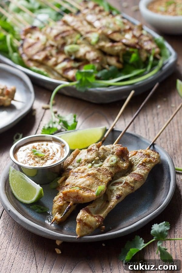 Thai chicken satay, marinated chicken threaded on bamboo skewers and grilled, on a gray plate served with peanut sauce and limes.