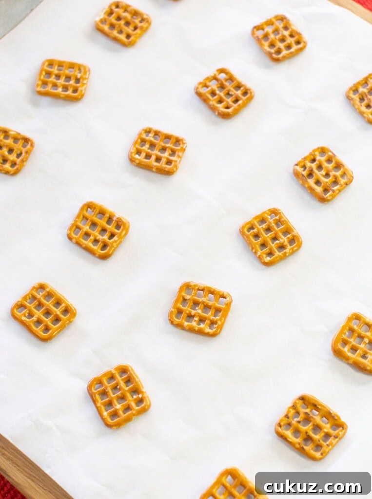 Square pretzels are spaced out on a sheet of white parchment paper, placed on a wooden surface.