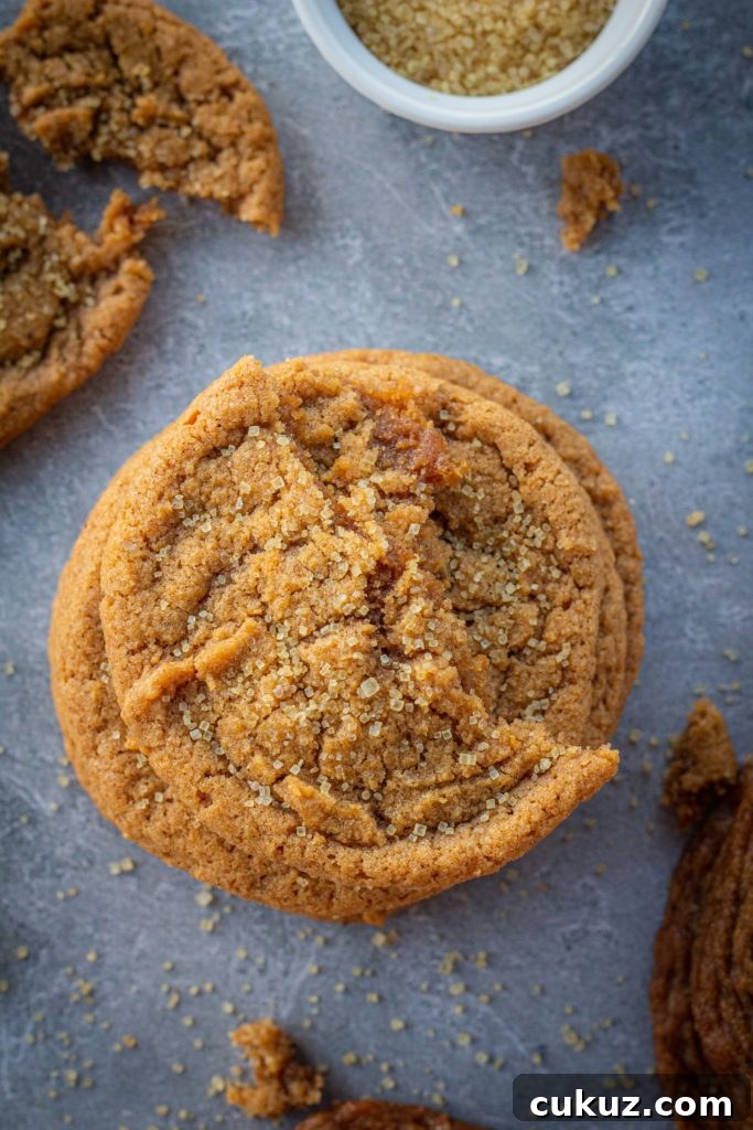 A stack of pumpkin cookies with half a cookie on top and crumbs surrounding it. Cookies are on a dark blue and white marbled backdrop and everything is sprinkled with coarse sugar.