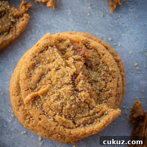 A stack of pumpkin cookies with half a cookie on top and crumbs surrounding it.