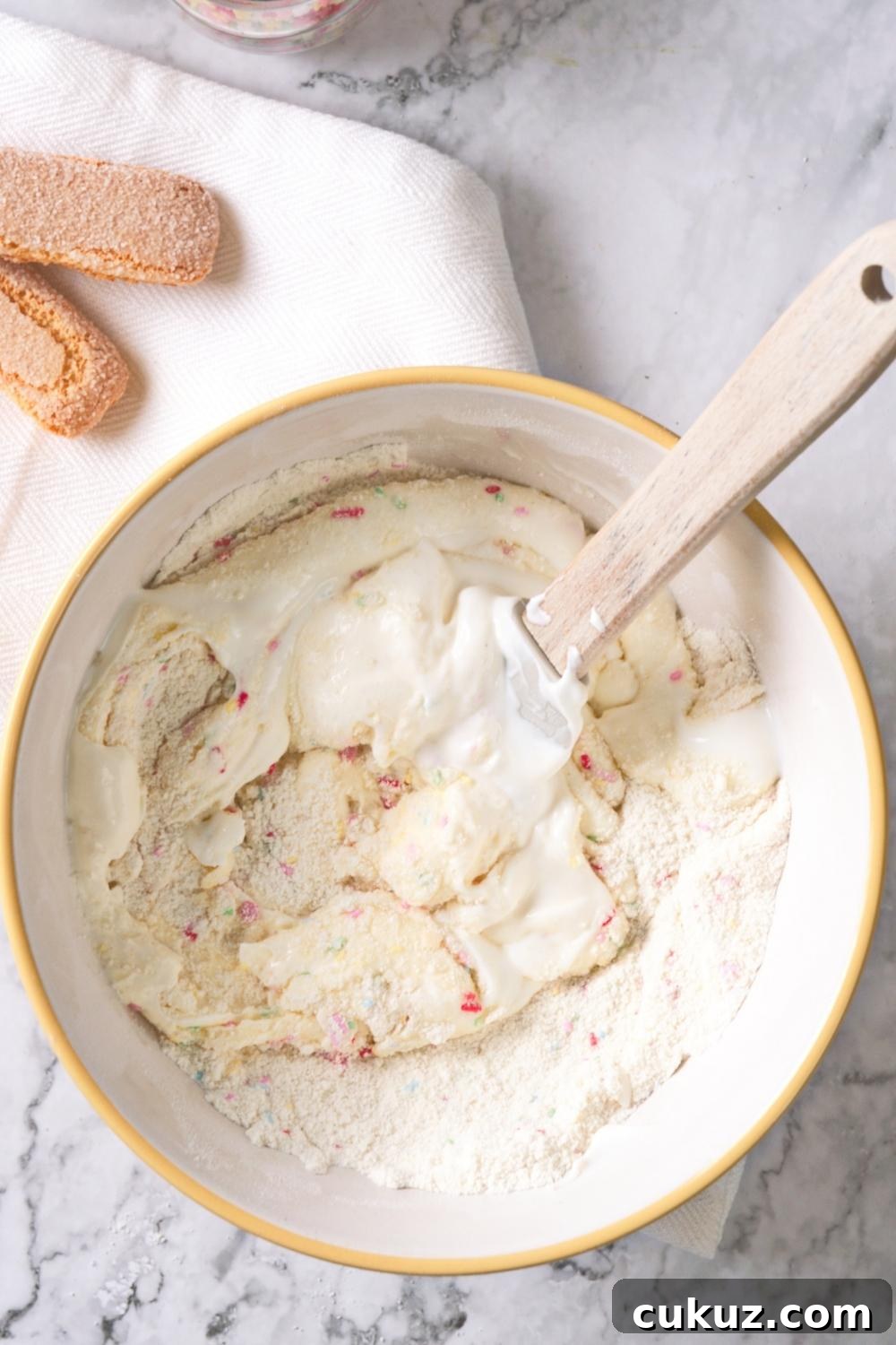 Quick 4-Ingredient Dunkaroo Dip Ready in 5 Minutes 5 An overhead view of a large mixing bowl with a spatula in it containing cake mix and yogurt.