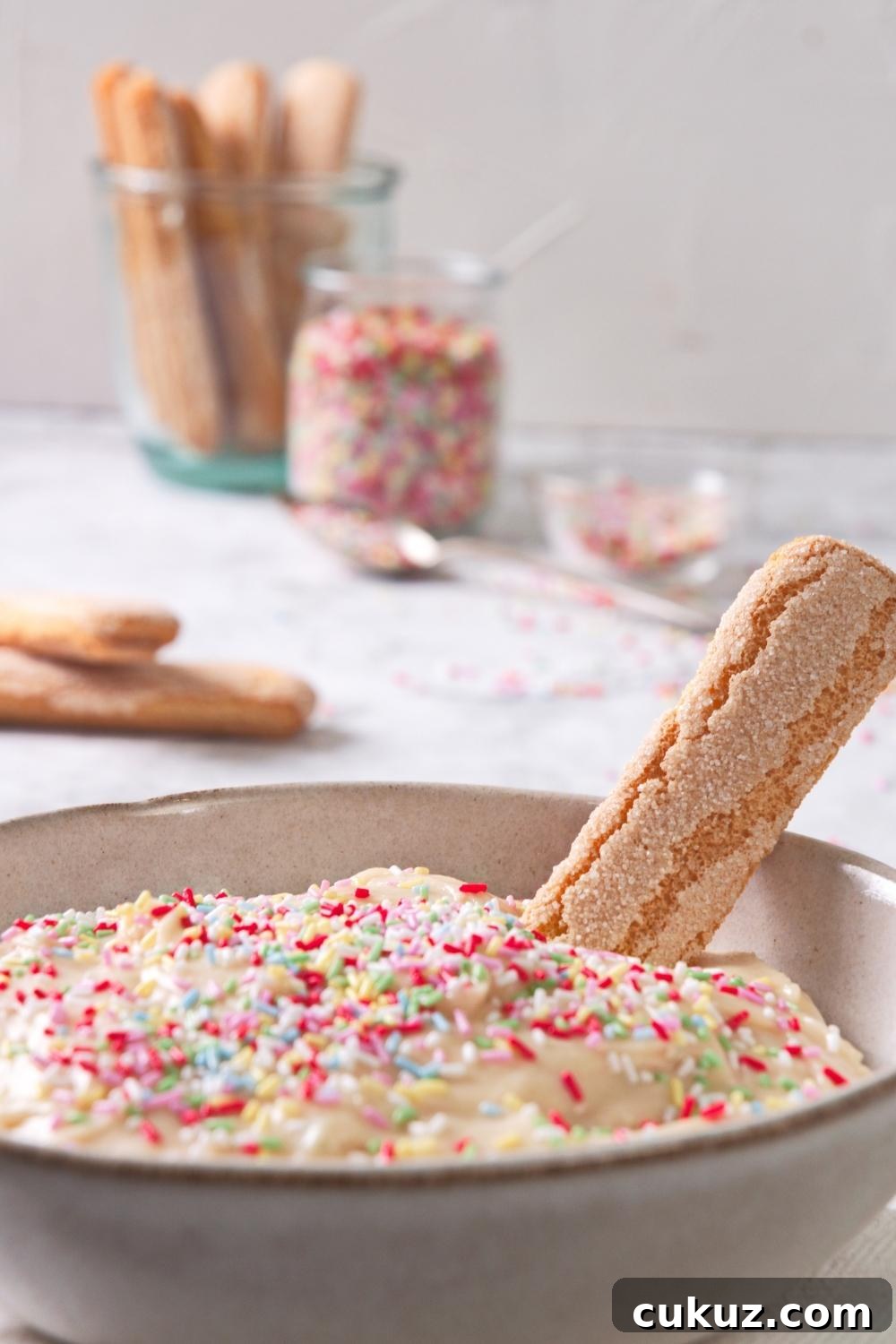 Quick 4-Ingredient Dunkaroo Dip Ready in 5 Minutes 9 A close-up of a serving bowl containing homemade Dunkaroo dip topped with rainbow sprinkles with a shortbread cookie dipped in it.