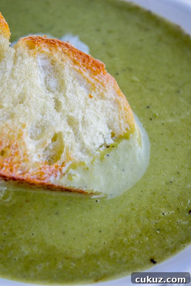 Creamy Frozen Pea Soup Ready in 30 Minutes 3 a baguette being dipped into homemade pea soup.