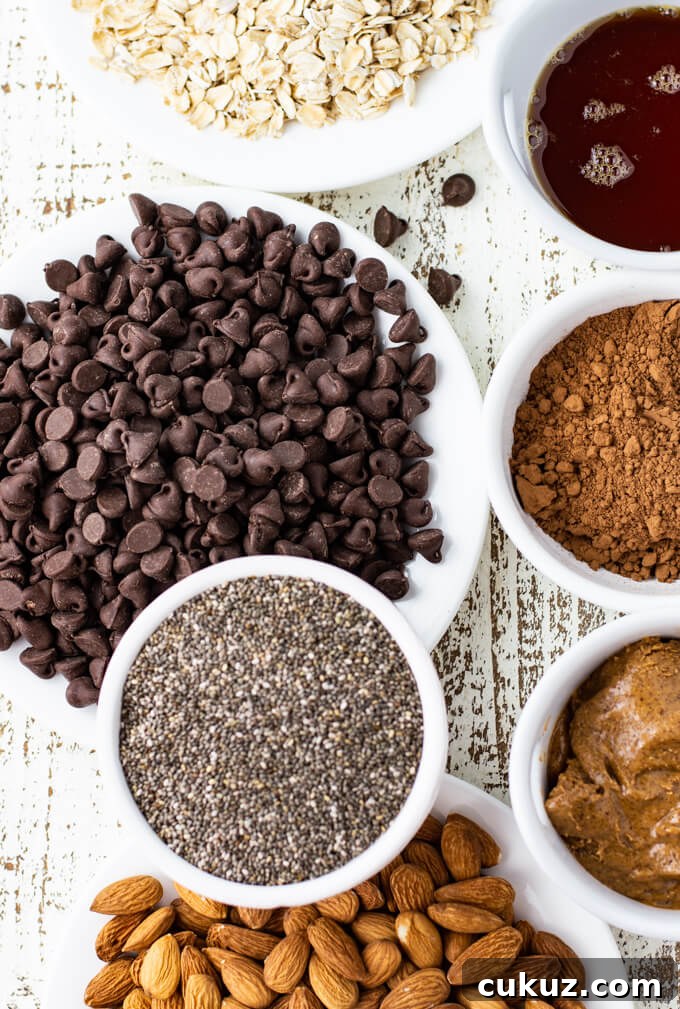 A white plate of chocolate chips with bowls that hold oats, honey, cocoa , almond butter, almonds and chia seeds.
