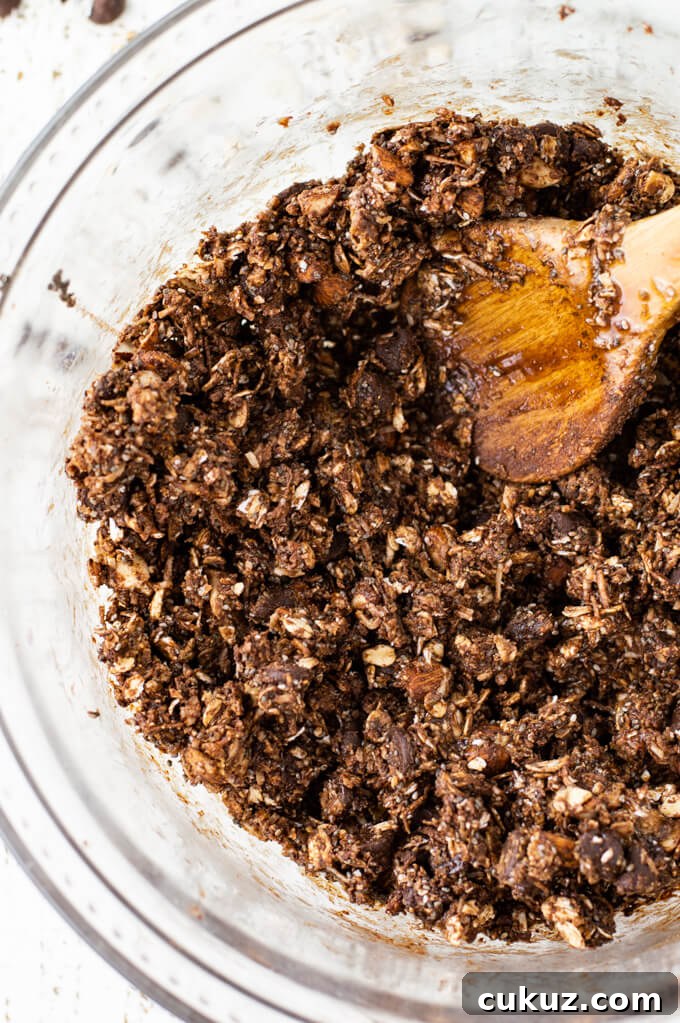 A clear mixing bowl with a mixture of almond joy energy balls. A wooden spoon sits in the middle of the mixture.