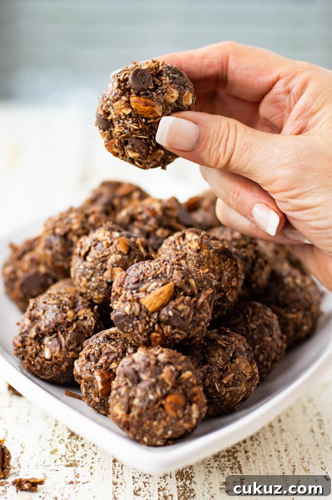 A white plate of Almond Joy Energy Balls. A hand is holding one ball up.