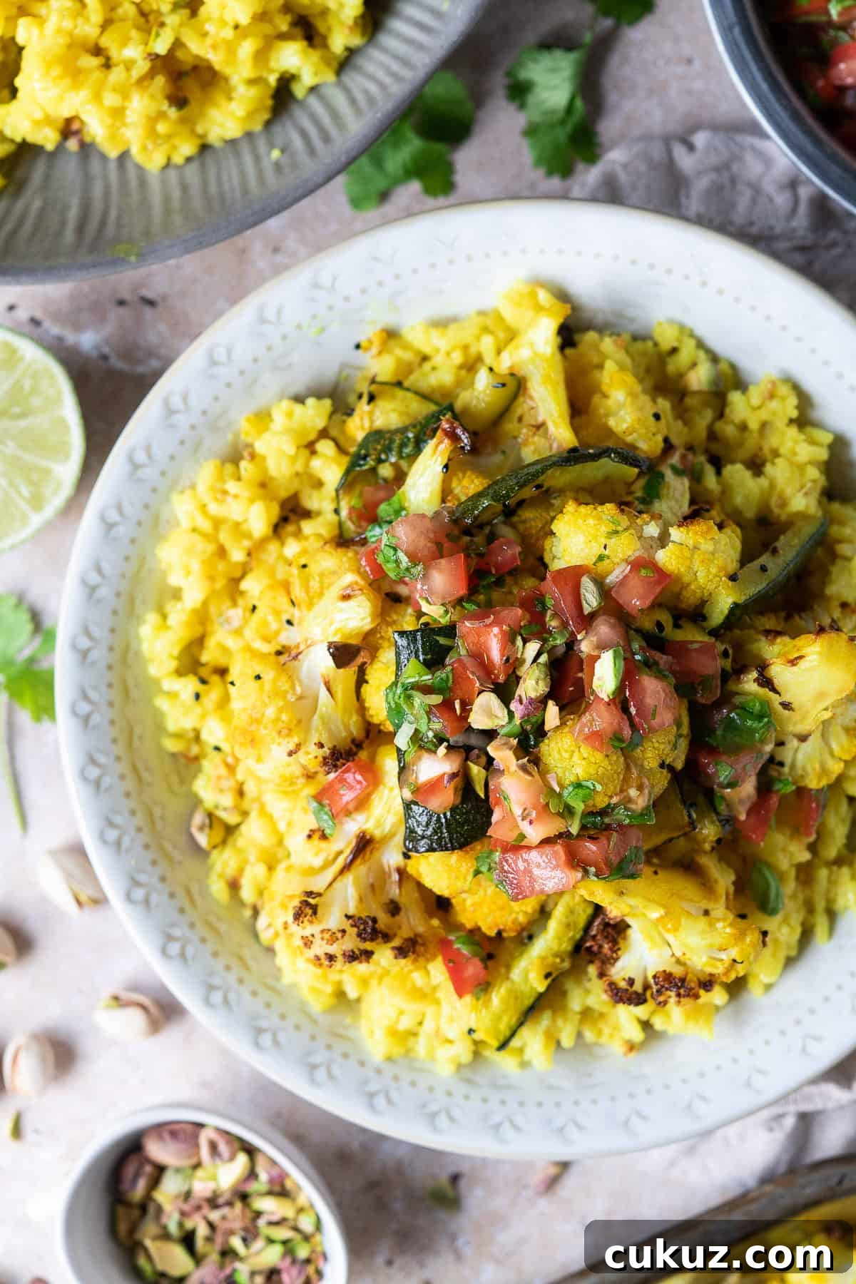 Close up of a white bowl of yellow rice topped with spiced roasted vegetables and tomato lime salsa.
