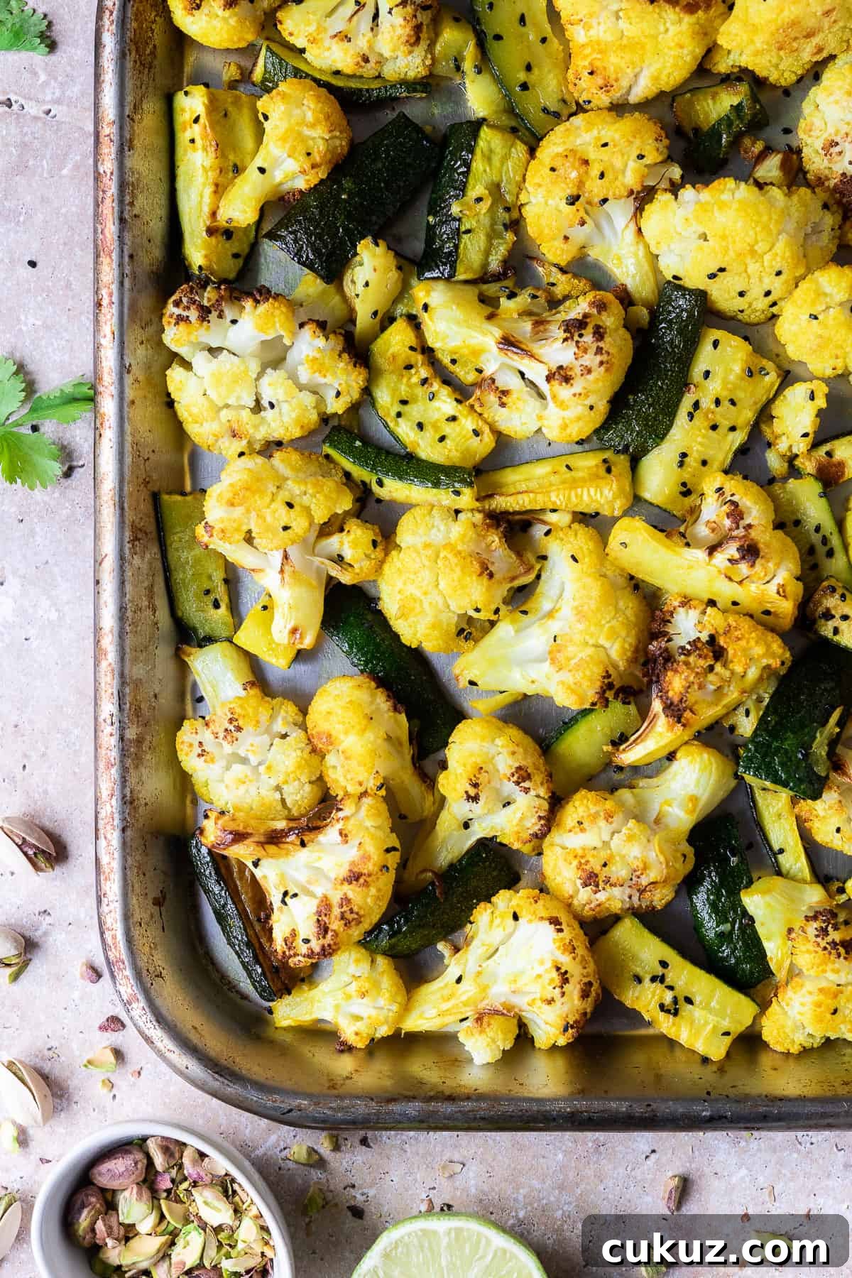 Close up of a metal roasting tray of spiced cauliflower and courgette.