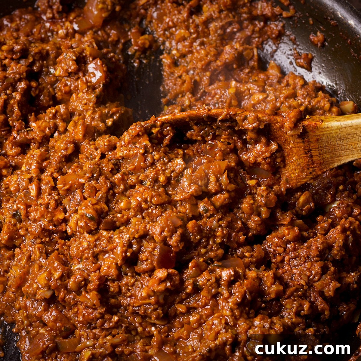 Someone using a wooden spoon to stir vegan taco meat while it cooks in a skillet.