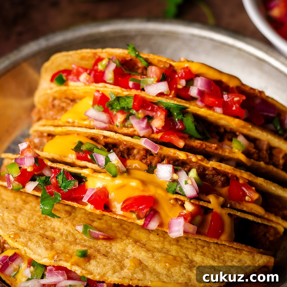 A tin plate filled with hard shell tacos stuffed with vegan taco meat, vegan nacho cheese, and pico de gallo.