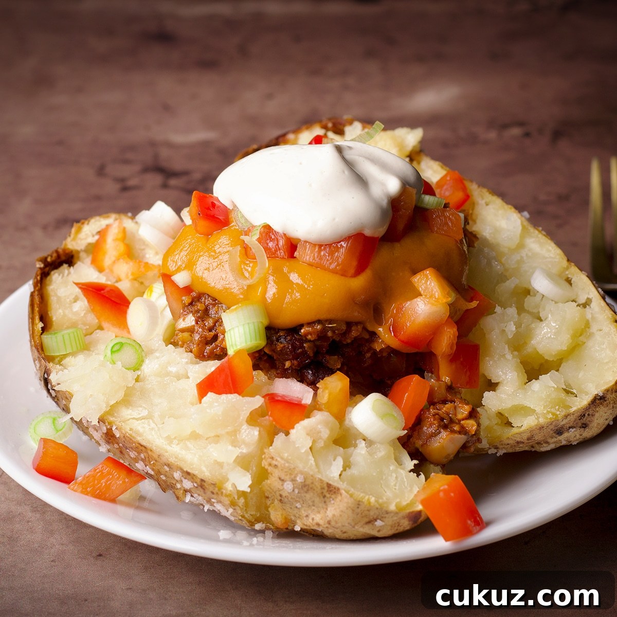A baked potato split in half and topped with vegan taco meat, vegan nacho cheese, vegan sour cream, and chopped veggies.