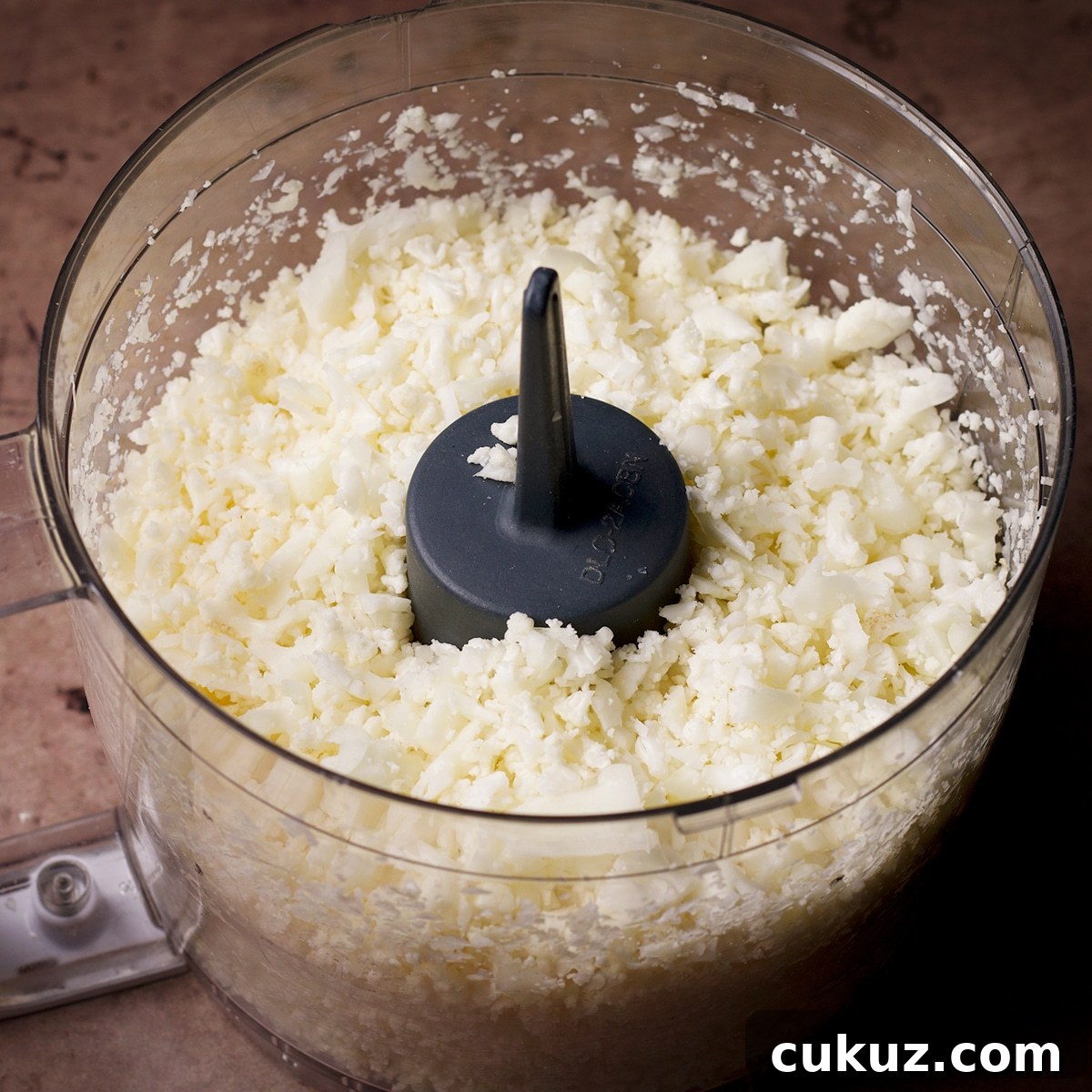 The bowl of a food processor filed with chopped cauliflower.