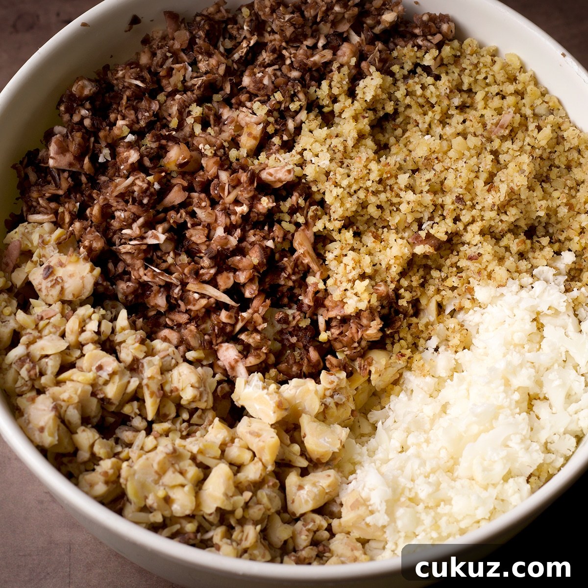 A white bowl filled with the chopped vegetables, tempeh, and walnuts needed to make vegan taco meat.