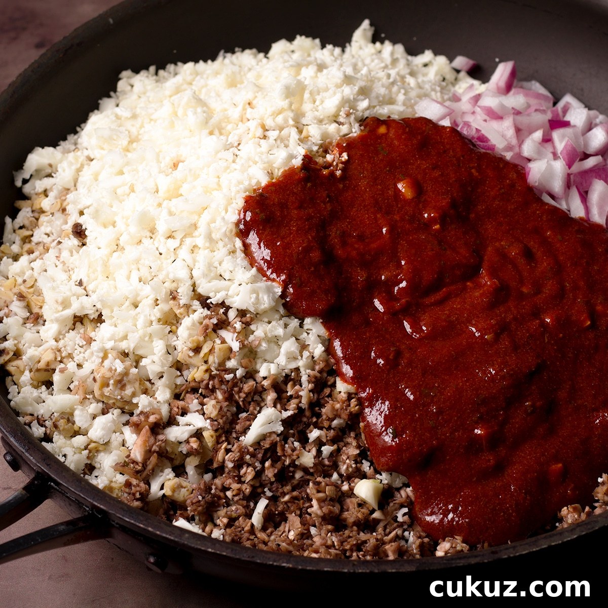 The chopped veggies, tempeh, walnuts, and Mexican adobo to make vegan taco meat piled into a skillet and ready to be cooked.