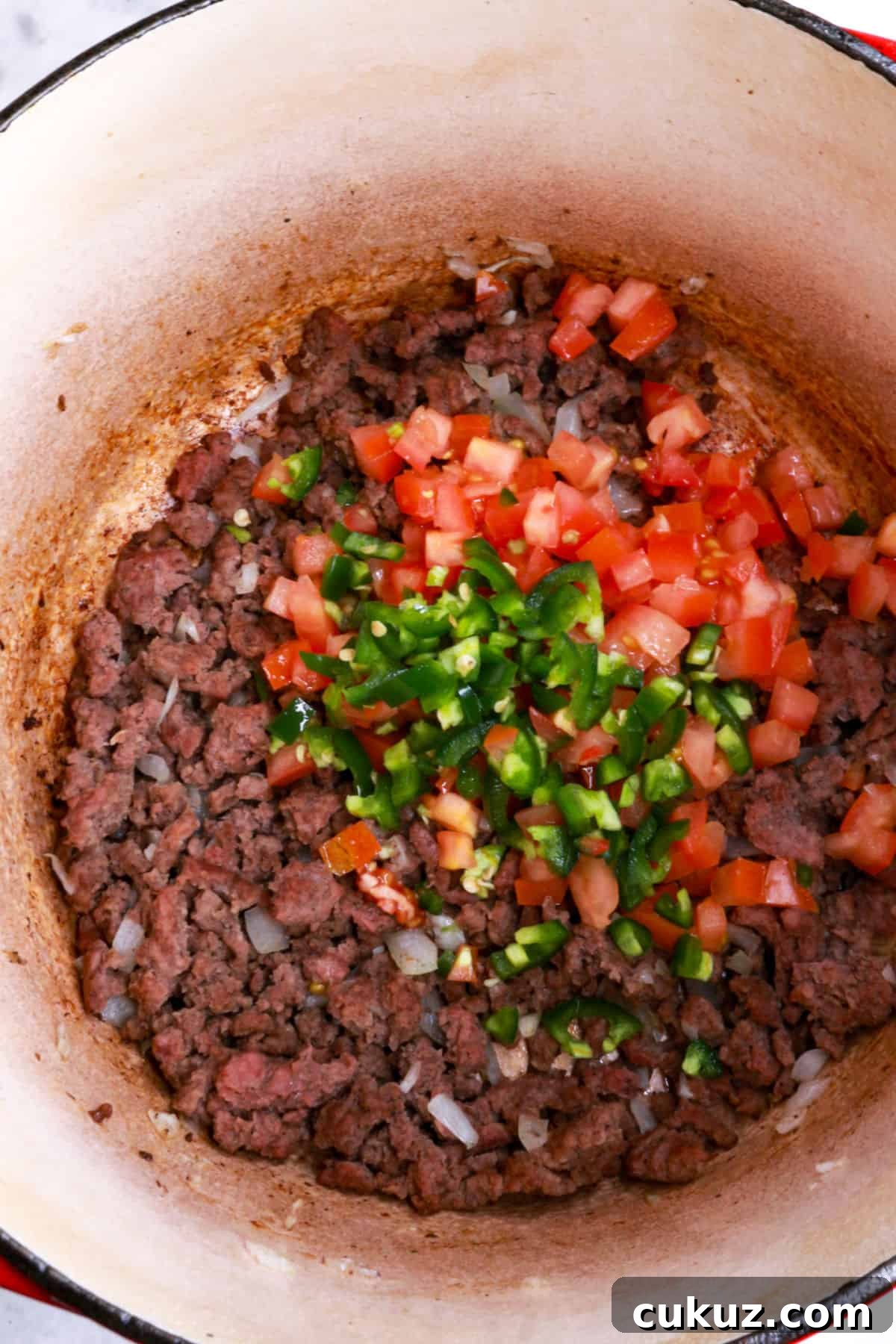 Diced tomato and jalapeño on browned ground beef in a pot