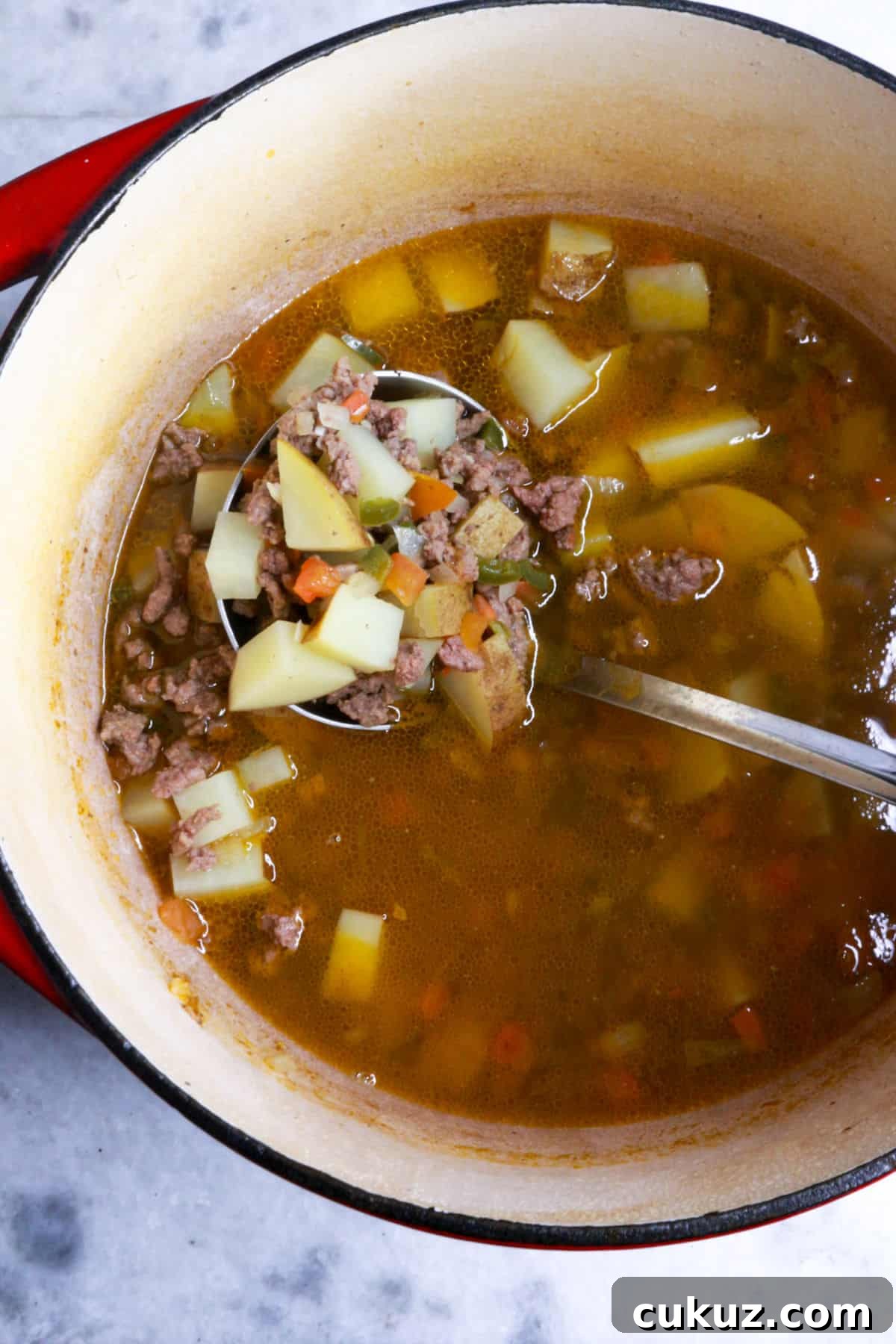 A ladle scooping ground beef stew with jalapeño