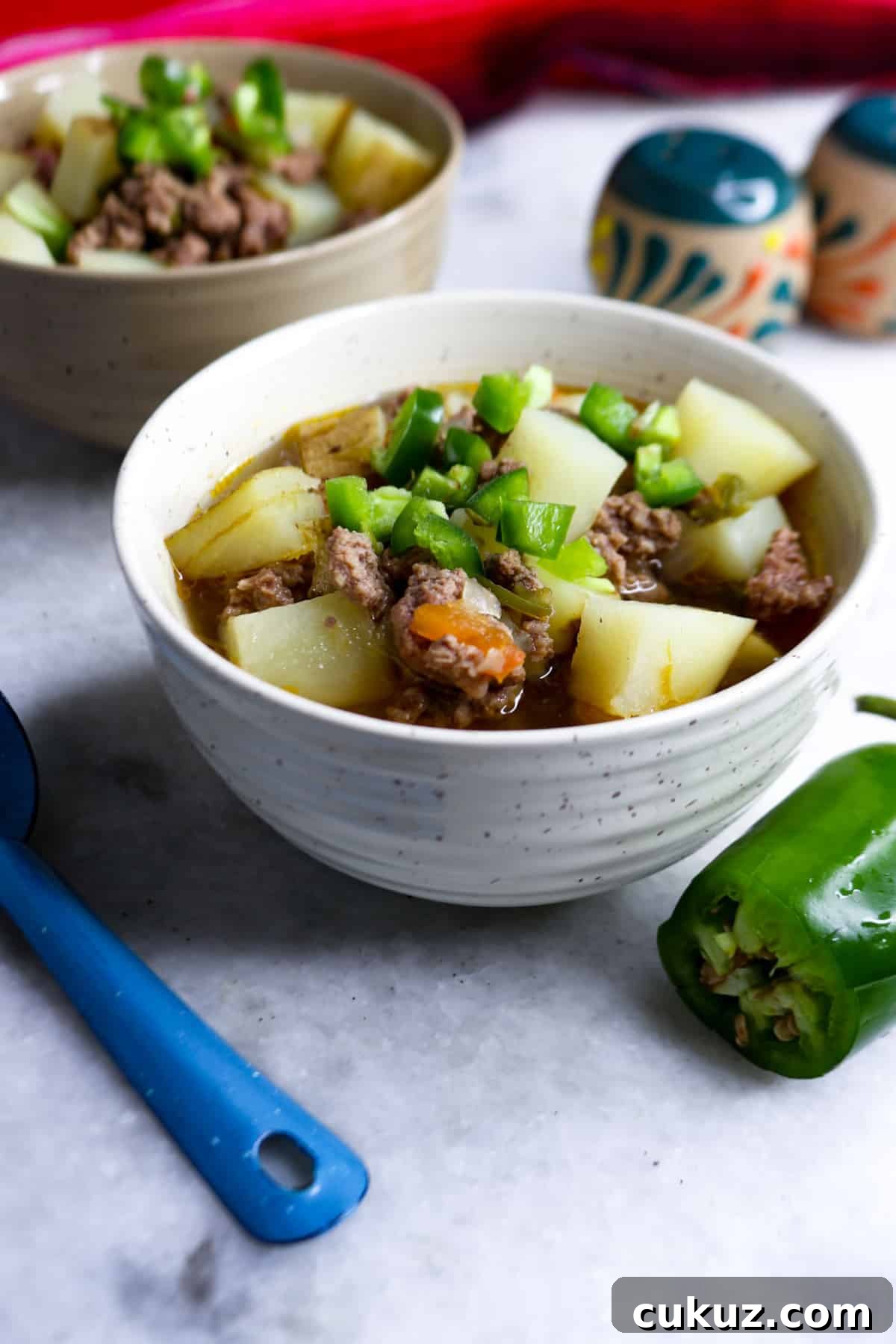 Caldillo de Carne Molida in a bowl with a jalapeño beside it and another bowl behind it