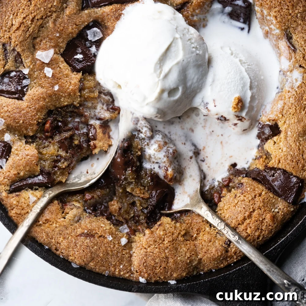 Two spoons eating gooey chocolate keto skillet cookie with melting vanilla ice cream