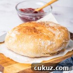 the air fryer bread on a wood cutting board set next to a blue checked kitchen towel and pot of jam.