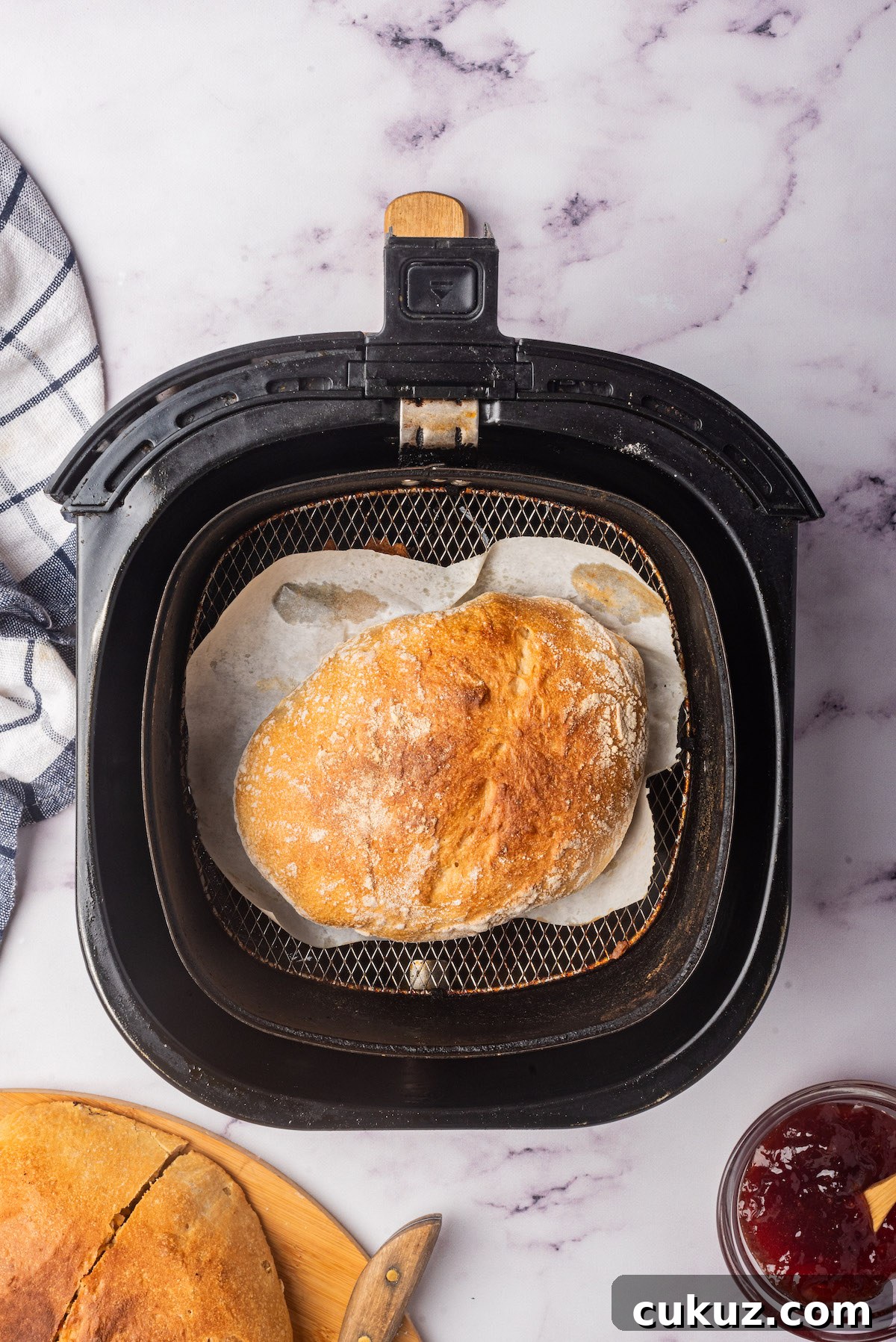 the baked bread inside the air fryer basket with a kitchen towel and pot of jam nearby.