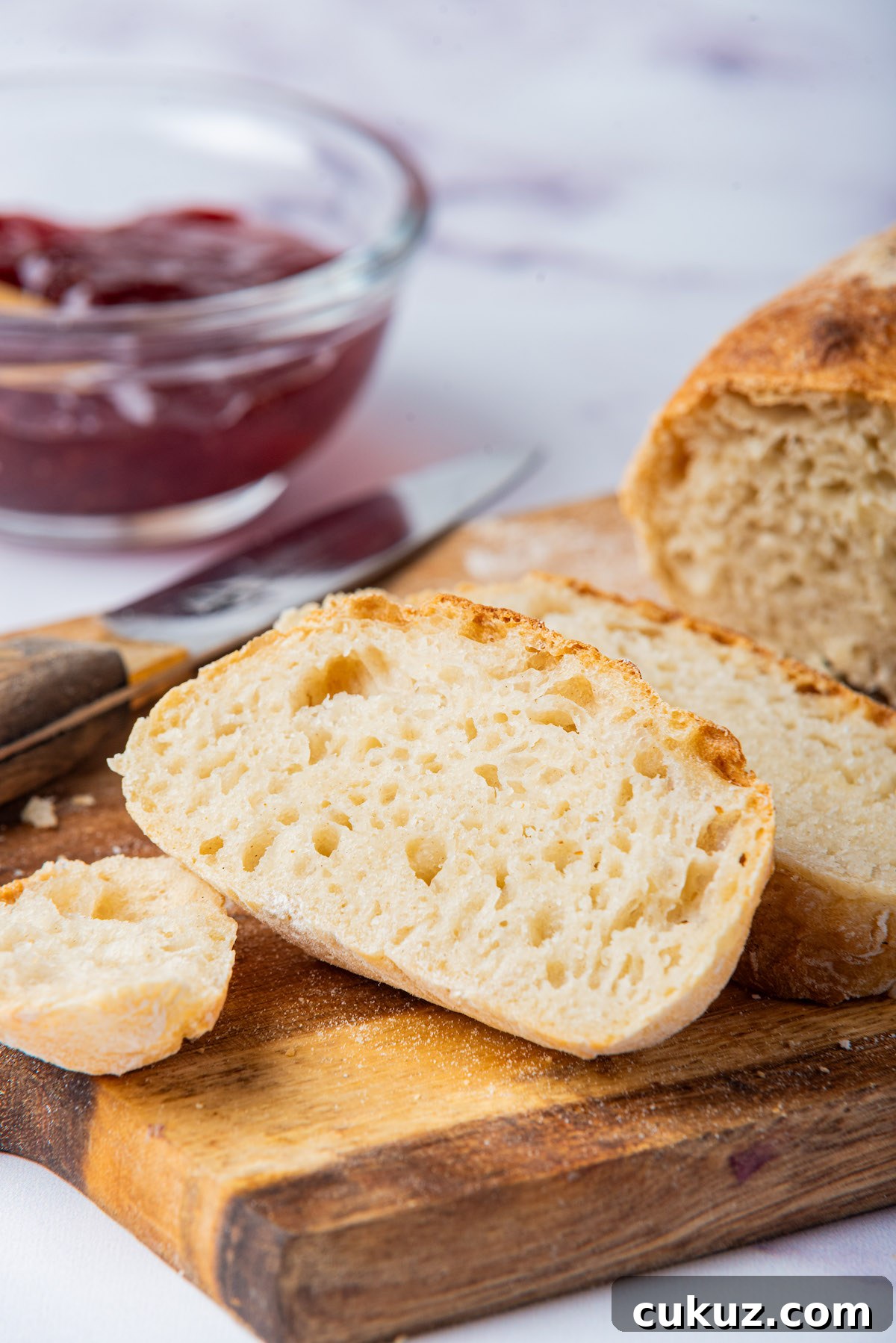 the sliced load of bread on a wooden serving board with a pot of jam and knife.