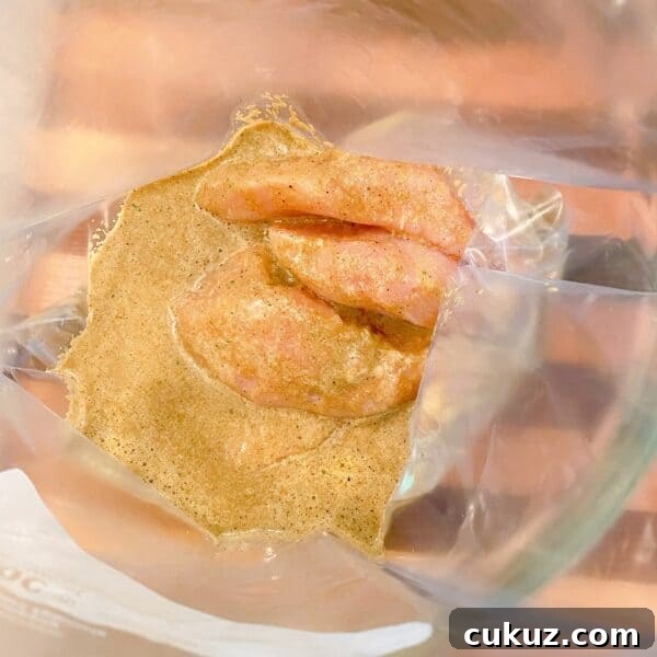 Large zip lock bag inside a big glass bowl with boneless skinless chicken breast and jerk marinade poured over it. Ready to marinade.