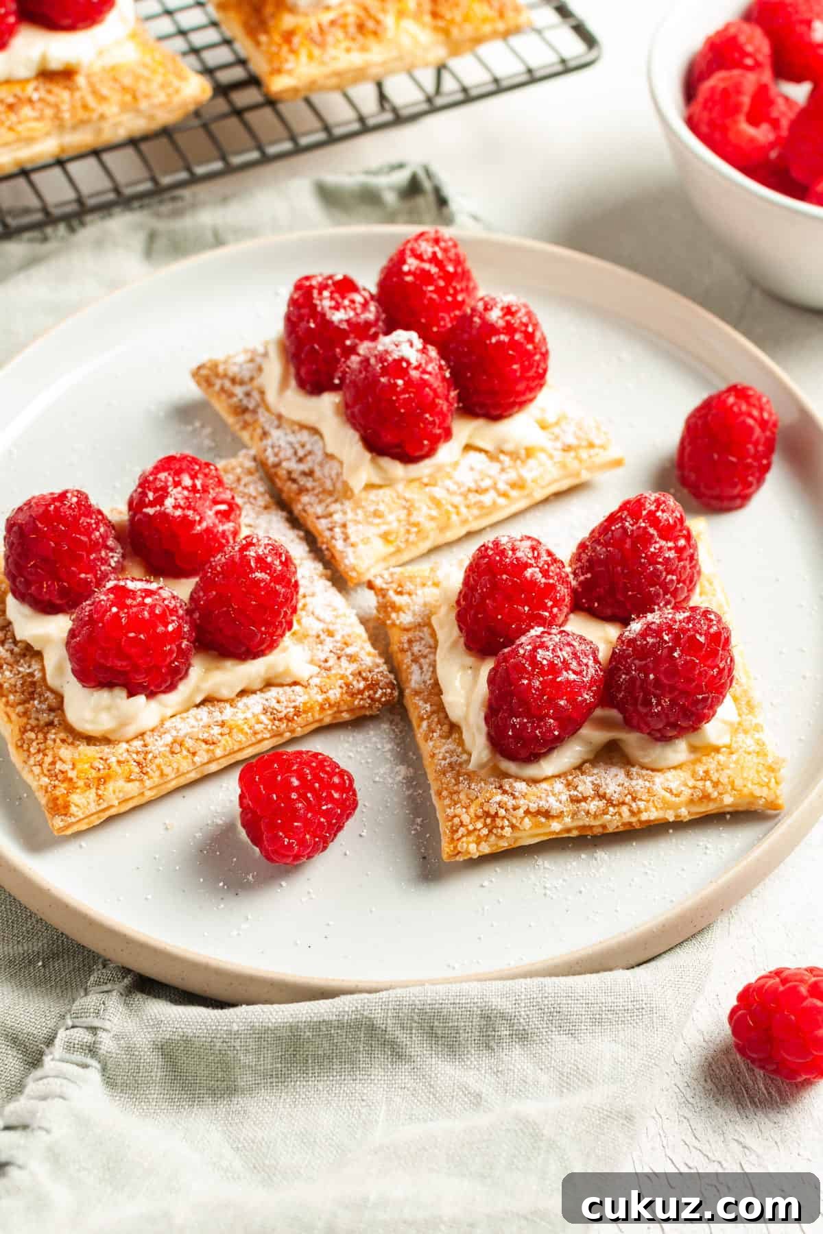 three tartlets sitting on a round white plate, with some raspberries around the edge.