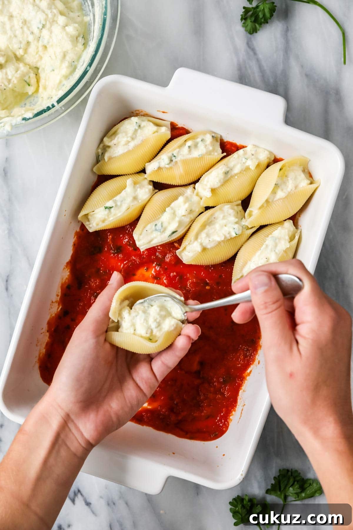 Overhead view of jumbo pasta shells being filled with a cheese filling and placed in a casserole dish with tomato sauce.