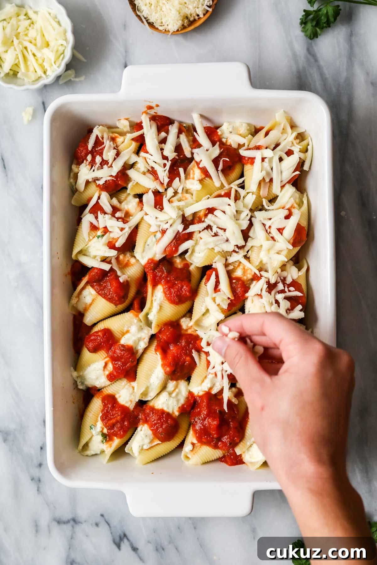 Overhead view of jumbo pasta shells being topped with sauce and shredded cheese.