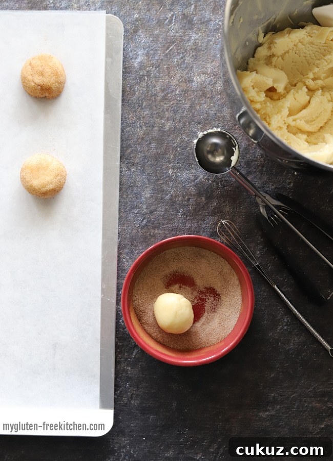 Some of the cookie balls coated in sugar and cinnamon with dough next to them.