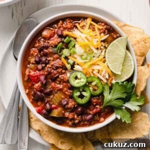 Hearty Beef and Bean Gluten-Free Chili Recipe 11 A bowl of chili garnished with cheese, jalapenos, green onion, and lime wedges.