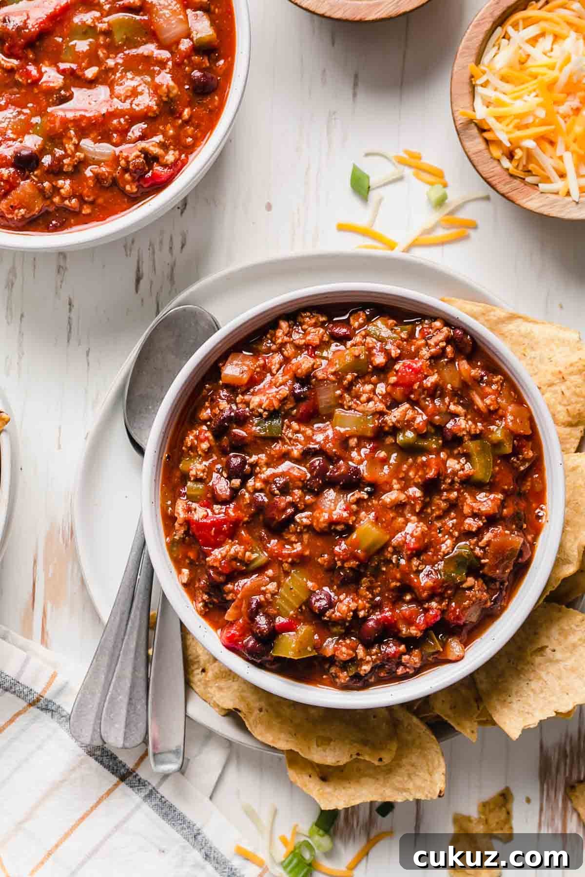 Hearty Beef and Bean Gluten-Free Chili Recipe 5 A bowl of gluten-free chili next to tortilla chips and shredded cheese.