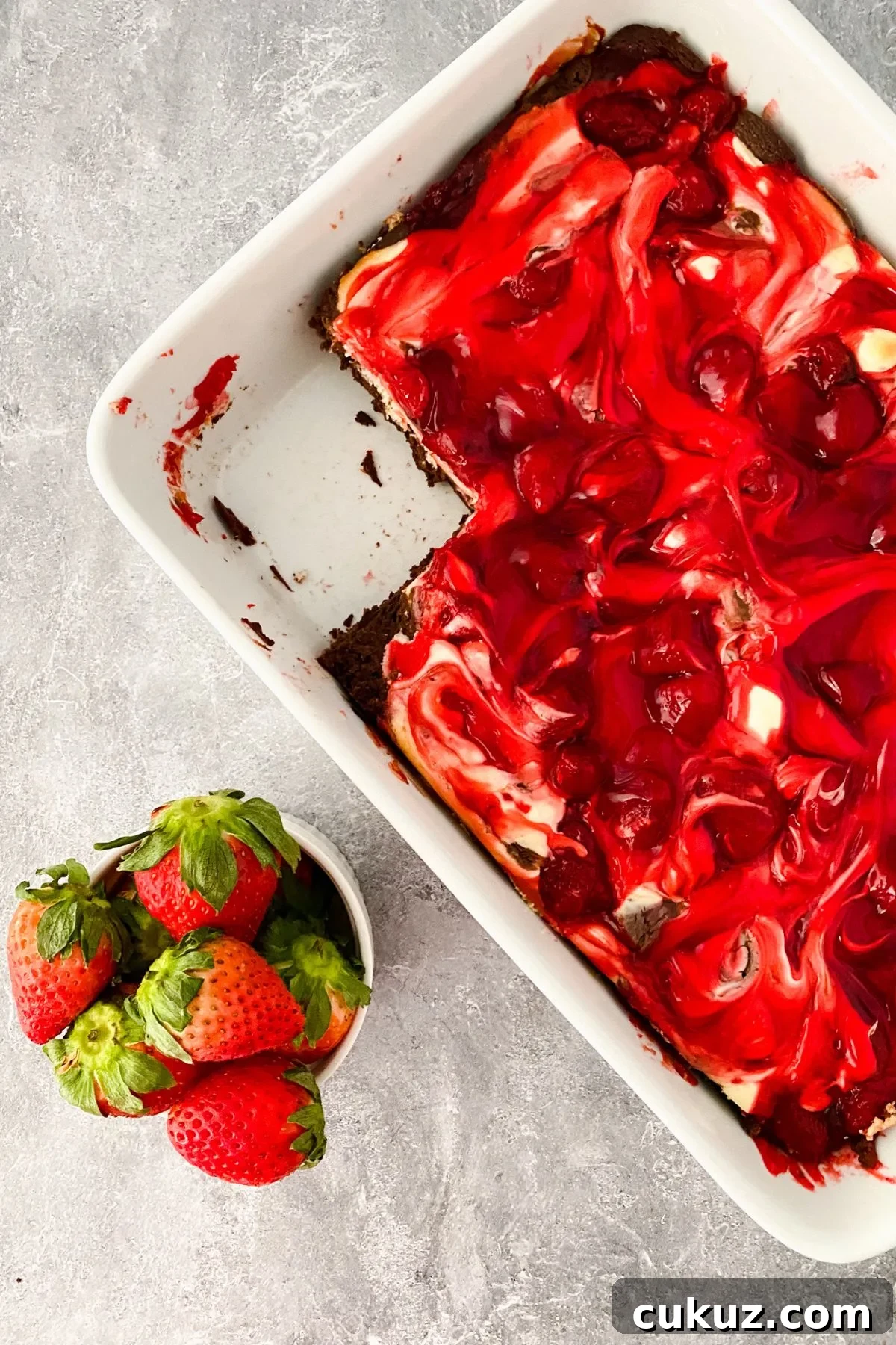 A baking dish of strawberry cheesecake brownies with a piece missing.