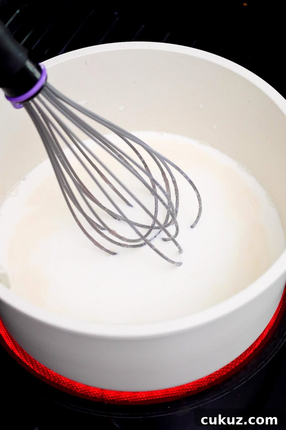 A whisk mixing half and half into the butter and flour mixture.