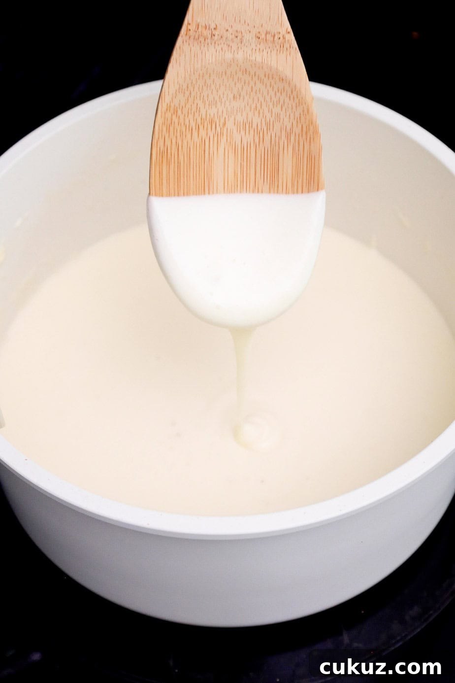 A spoon lifted from a pot of thickened cheese sauce.