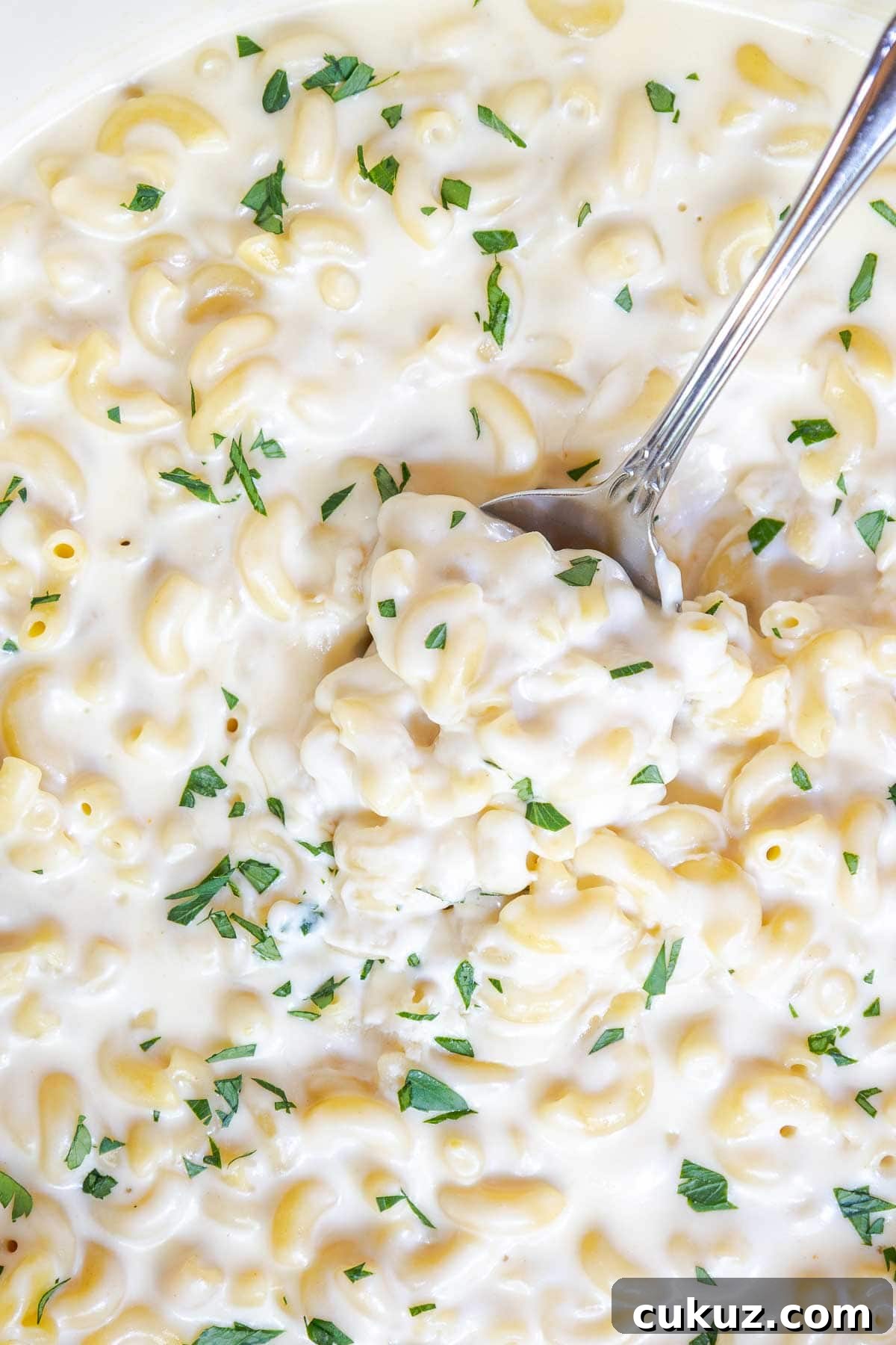 A spoon scooping white cheddar mac and cheese from a pot, garnished with parsley.