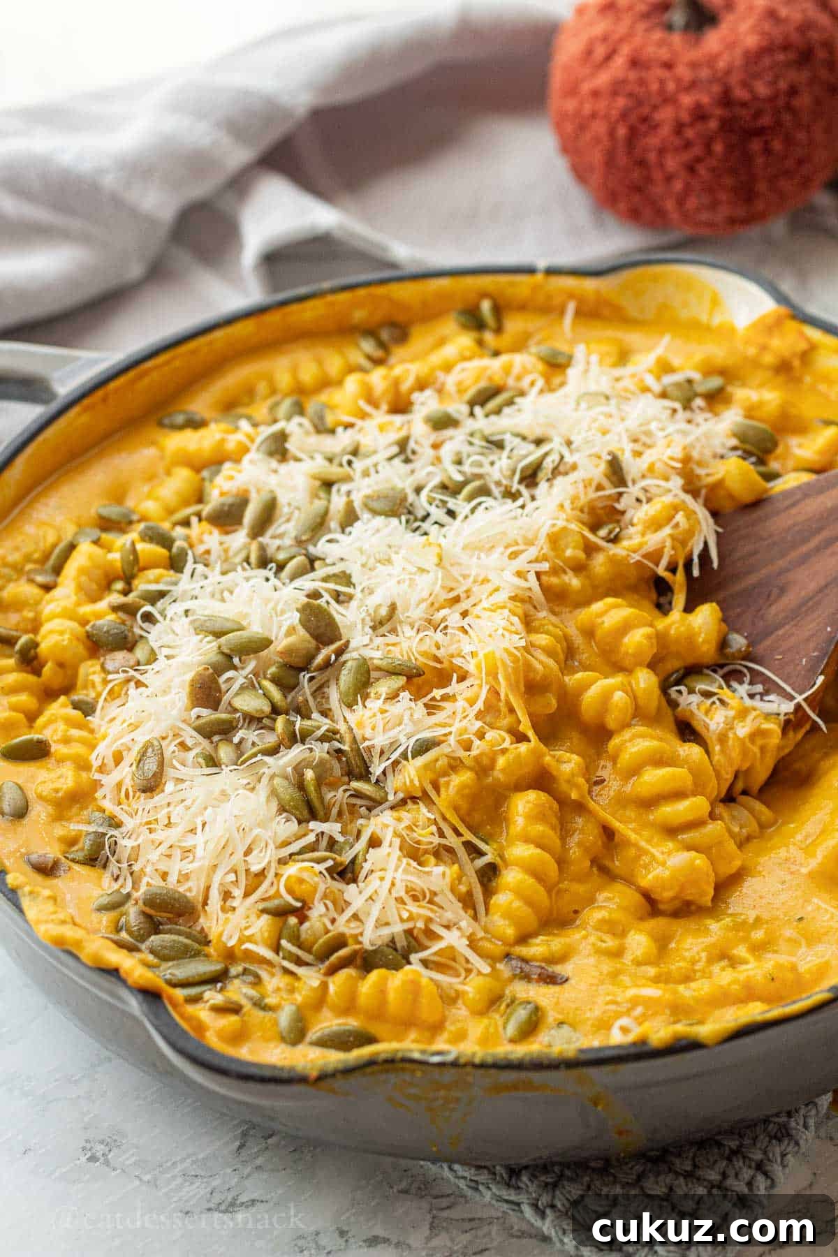 Pumpkin pasta with parmesan and pepitas in pan with wooden spatula.