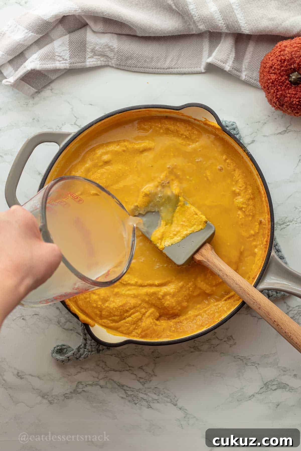 Pouring pasta water into pan with pumpkin sauce.