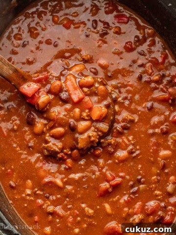 Cooked ladleful of turkey chili in black crockpot.