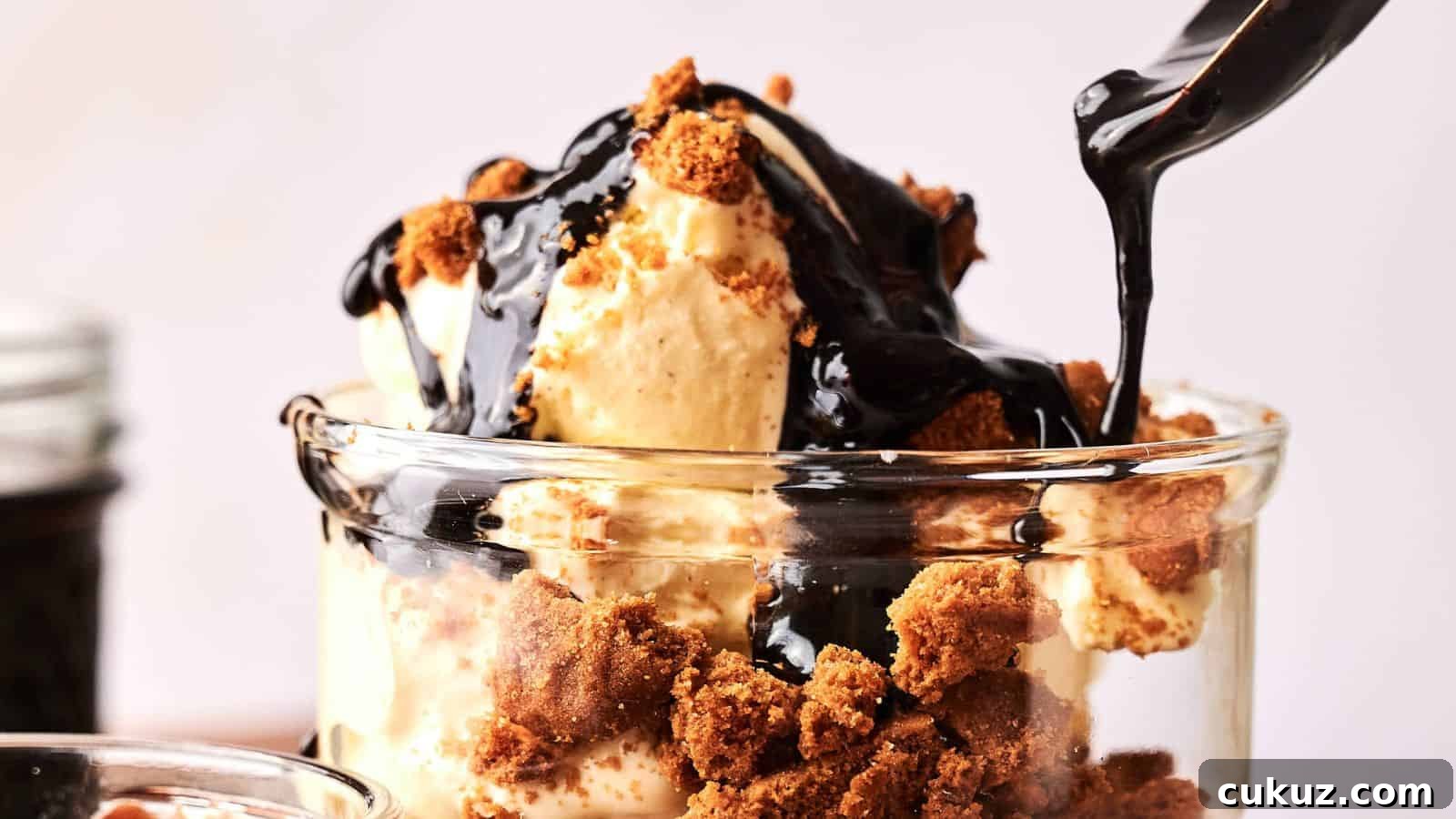 A glass filled with vanilla ice cream, crumbled cookies, and chocolate sauce being poured on top.