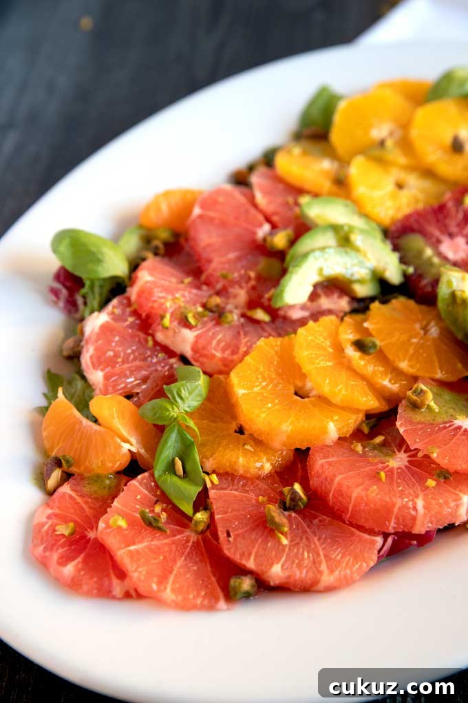 Peeled and sliced citrus fruit, oranges, grapefruit, pomelos with avocado slices and basil leaves on a white plate.