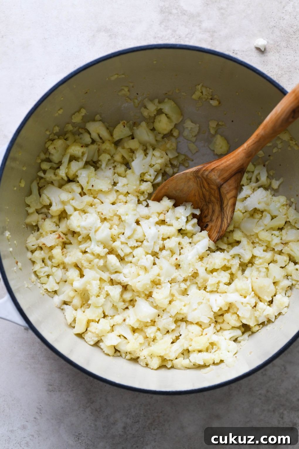 Overhead shot of cooked cauliflower inside large white ceramic dutch oven, on a light grey background. 